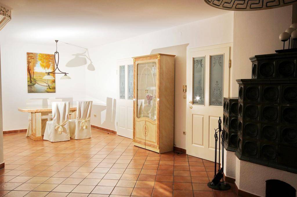 Essbereich mit traditionellem Kachelofen, Esstisch und einem eleganten Vitrinenschrank.