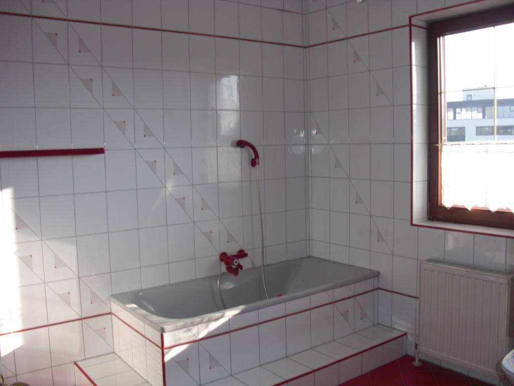 Badezimmer mit weißen Fliesen, roten Akzenten, eingebauter Badewanne und Fenster.