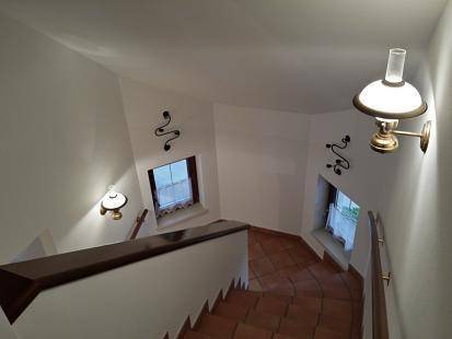 Treppenhaus von oben gesehen mit gefliesten Stufen und dekorativen Wandleuchten.
