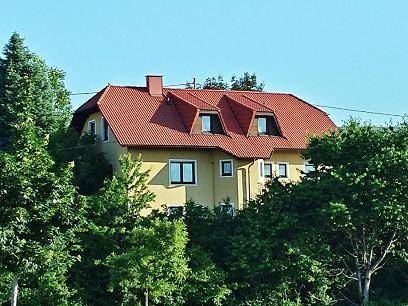 Das gelbe Haus mit rotem Dach, umgeben von üppigem Grün und Bäumen.