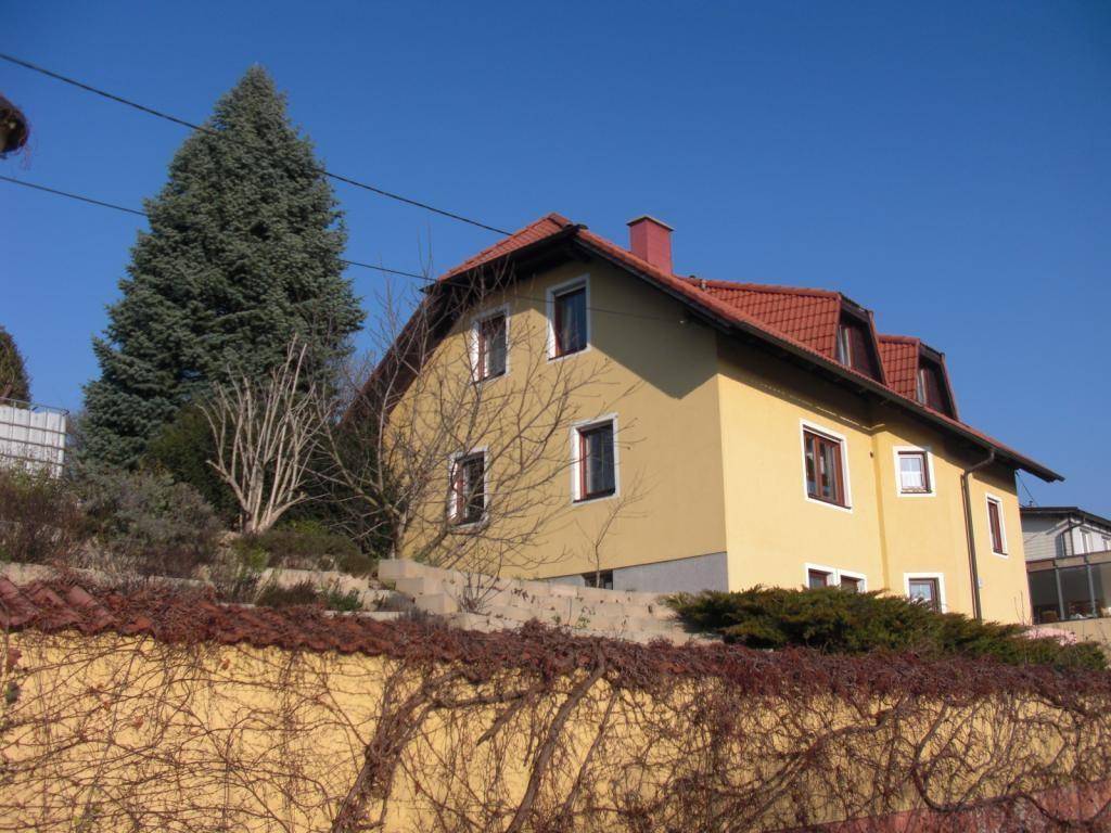 Seitenansicht des Hauses mit Hanglage, umgeben von Bäumen und Sträuchern.