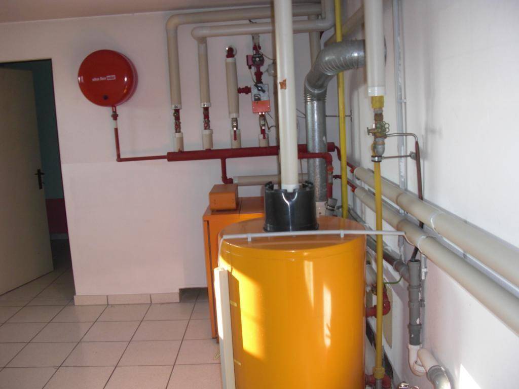 Heizungsraum mit Warmwasserspeicher und sichtbaren Rohrleitungen, funktional eingerichtet.