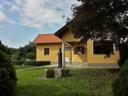 Gartenbereich mit traditioneller Wasserpumpe, umgeben von Rasen und Bäumen.