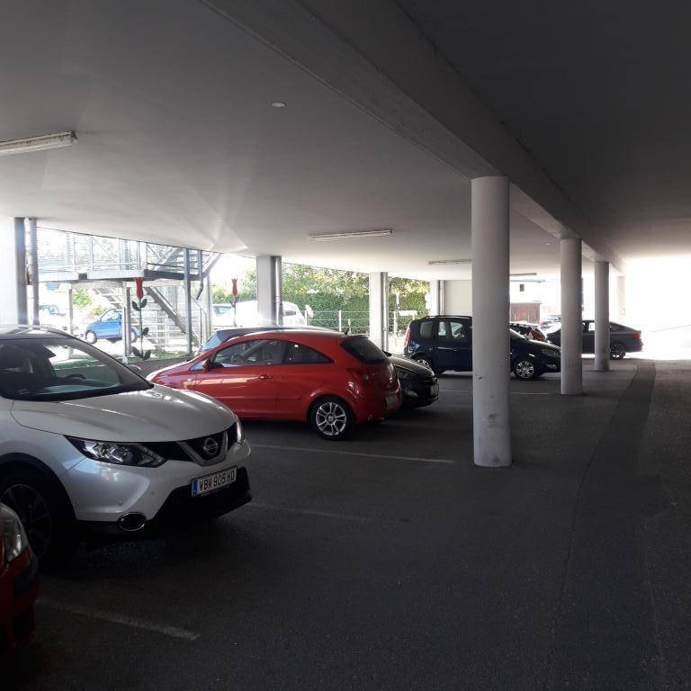 Überdachter Parkbereich mit mehreren geparkten Fahrzeugen und tragenden Säulen, der gut beleuchtet ist.