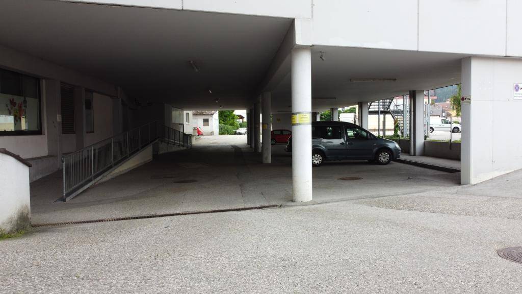 Überdachter Parkbereich mit einer Rampe für Fahrzeuge und einem hellen Ausgang im Hintergrund, der gut zugänglich ist.