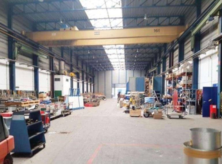 Große Industriehalle mit Betonboden, Oberlichtern und einem gelben 16-Tonnen-Kran, der über den Arbeitsbereich ragt.