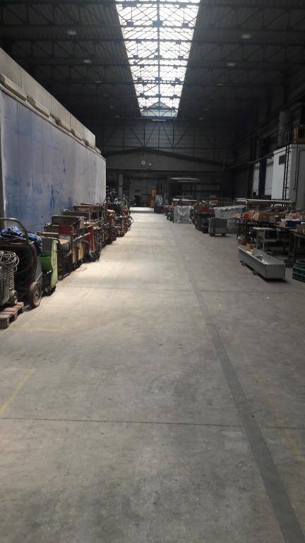 Geräumige Lagerhalle mit Betonboden und einer Reihe von Maschinen und Geräten entlang der Wand unter Oberlichtern.