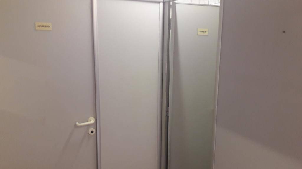 Zwei schlichte Toilettenkabinen mit hellgrauen Türen und einfachen Beschriftungen in einem Sanitärbereich.