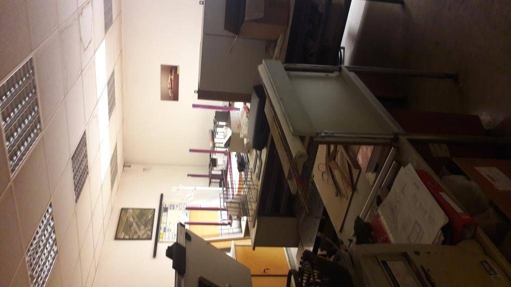 Unaufgeräumtes Büro mit mehreren Schreibtischen, Büromöbeln und Deckenleuchten, die den Raum erhellen.