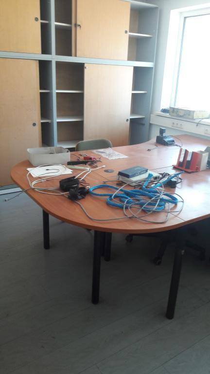 Büro mit einem großen, geschwungenen Holztisch voller Kabel und einem Einbauschrank an der Wand.