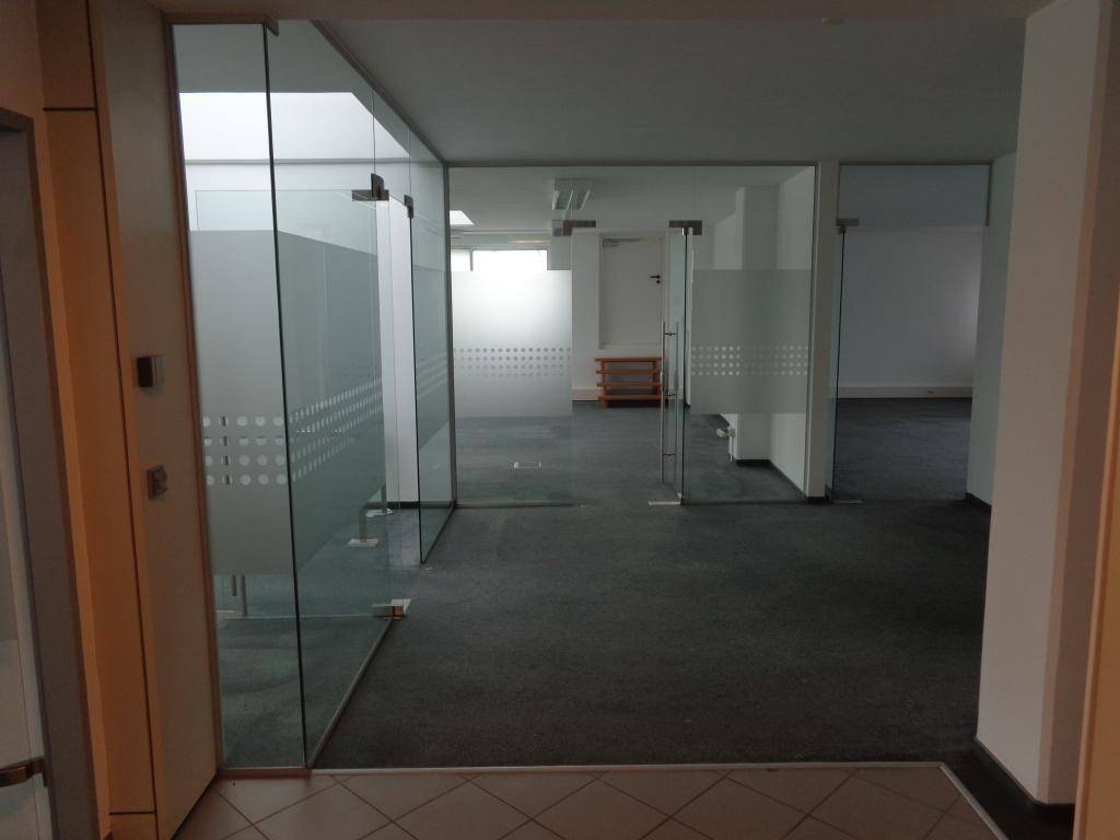 Leerer Büroraum mit modernen Glaswänden und Teppichboden, der eine offene und helle Arbeitsumgebung schafft.