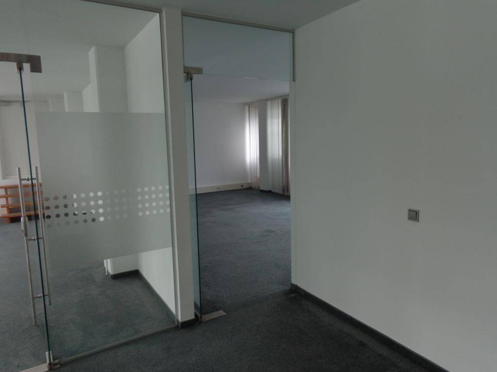 Heller Bürobereich mit Glaswänden und Teppichboden, der viel Tageslicht durch die Fenster hereinlässt.