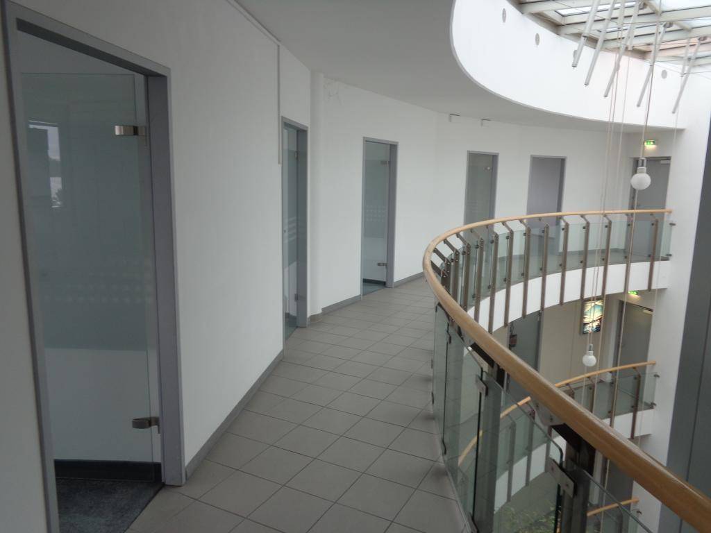 Geschwungener Flur mit Glasgeländer und Blick auf ein mehrstöckiges Atrium, das eine offene und helle Atmosphäre schafft.