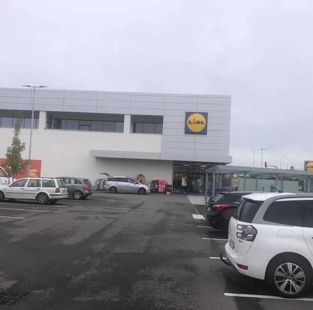 Eingangsbereich des modernen Supermarktes mit angrenzendem Parkplatz und Einkaufswagen.