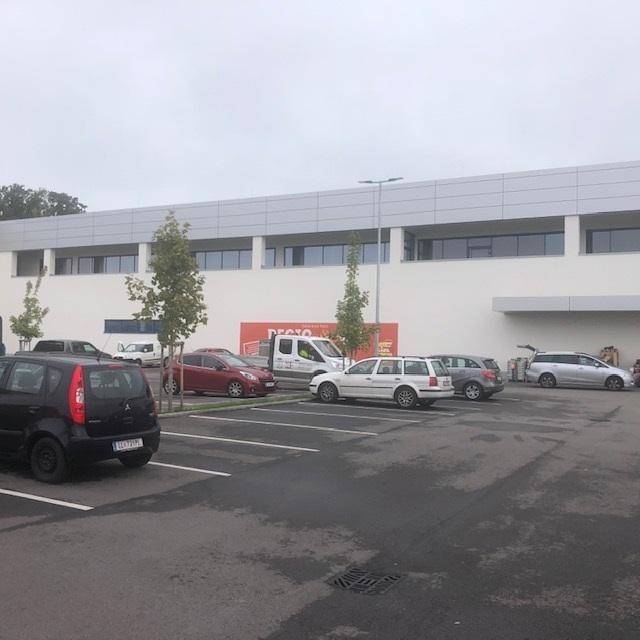 Seitenansicht des Supermarktgebäudes mit weiteren Parkplätzen und geparkten Fahrzeugen.