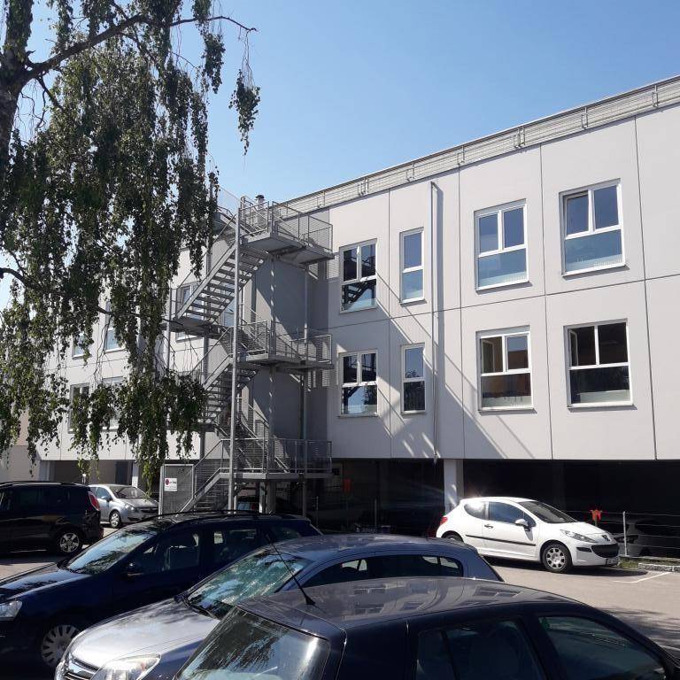 Seitenansicht des Gebäudes mit einer externen Metalltreppe und geparkten Autos im Vordergrund unter blauem Himmel.