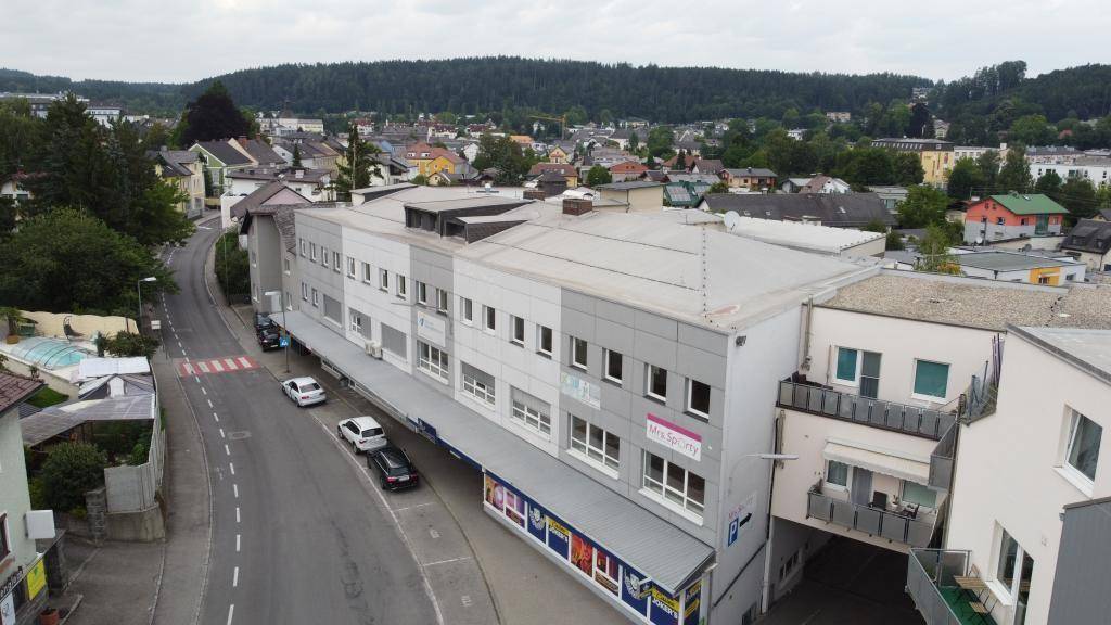Luftaufnahme des Geschäftsgebäudes mit umliegenden Wohnhäusern und einer bewaldeten Hügellandschaft im Hintergrund.