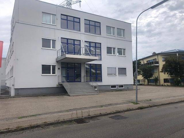 Ansicht eines modernen Bürogebäudes mit blauen Fenstern, Balkon und Parkmöglichkeiten davor.