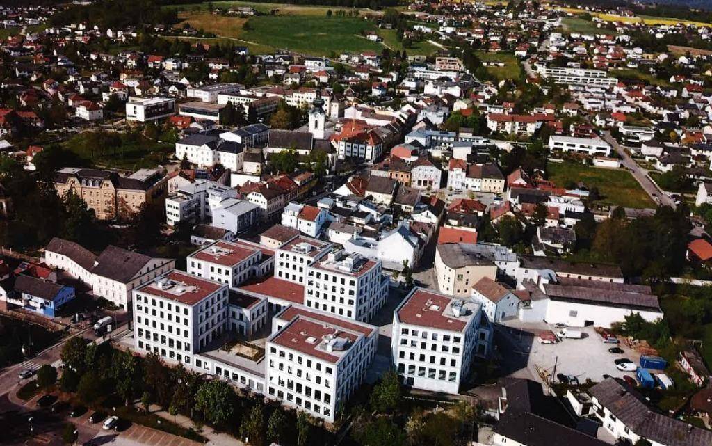 Luftaufnahme eines modernen Gebäudekomplexes in einer städtischen Umgebung mit vielen Häusern und Grünflächen.