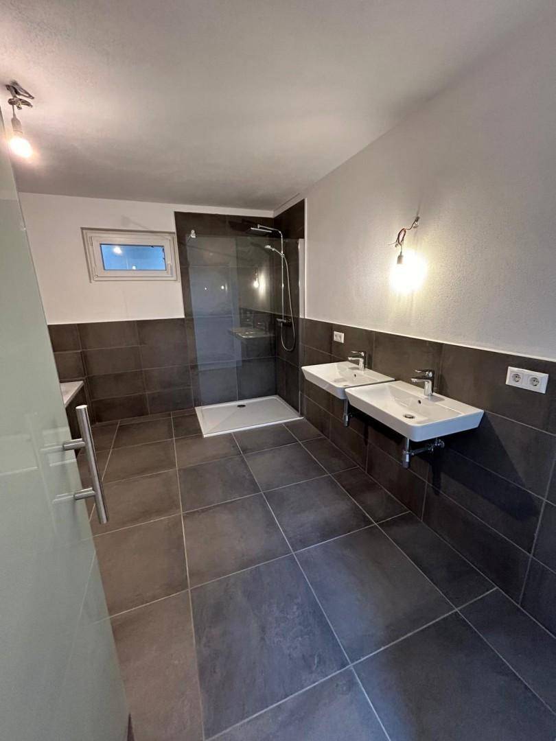 Modernes Badezimmer mit dunklen Fliesen, zwei Waschbecken und großer begehbarer Dusche.