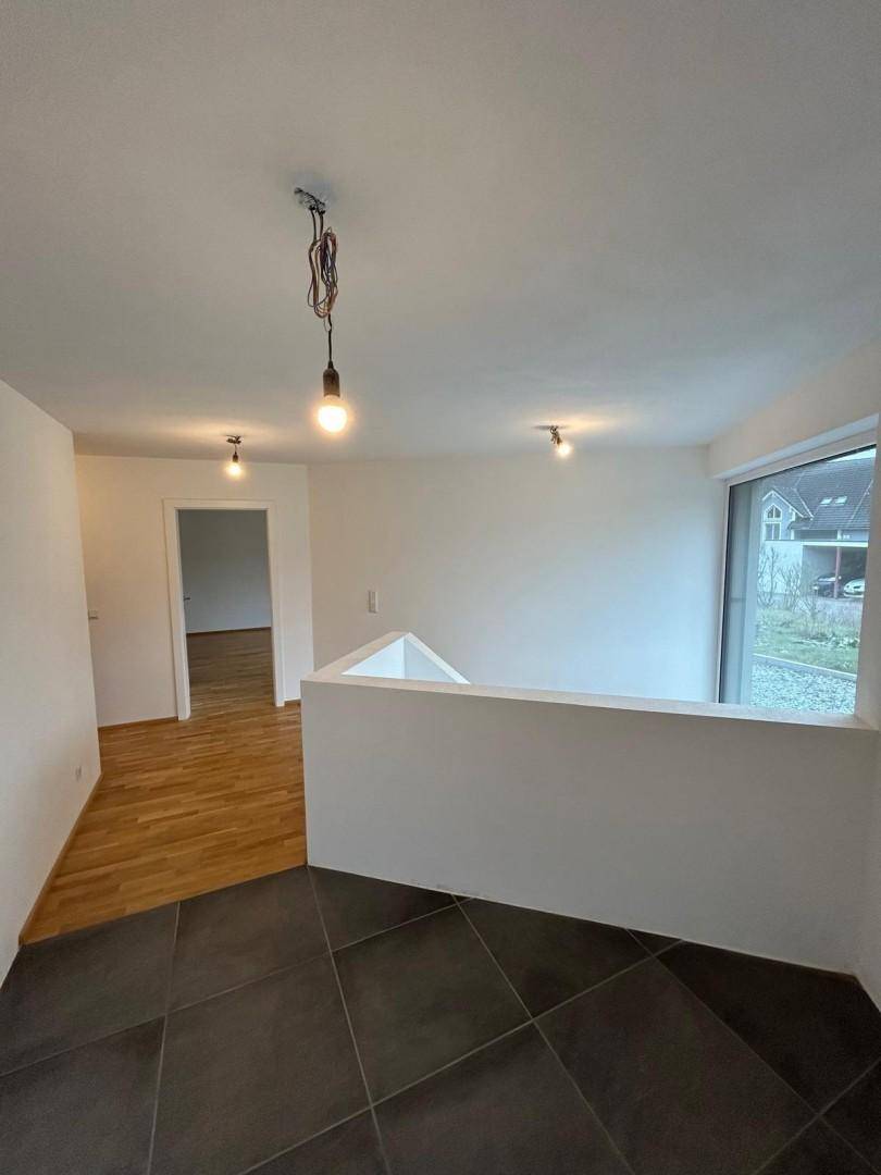 Obergeschoss-Flur mit Holzparkett und dunklen Fliesen, offenem Treppenbereich und Fenster.