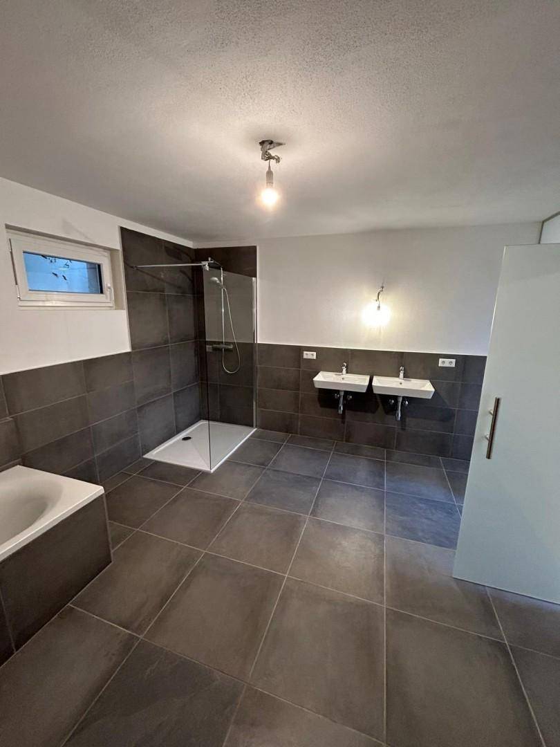 Modernes Badezimmer mit dunklen Fliesen, zwei Waschbecken, Dusche und Badewanne.