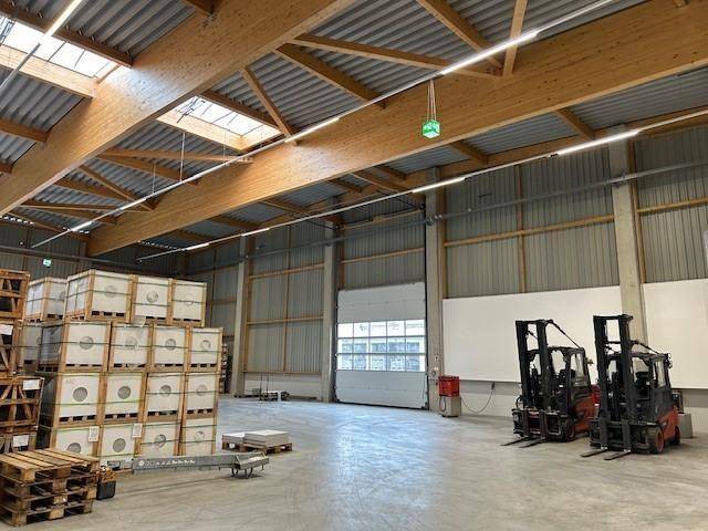 Innenansicht einer Lagerhalle mit Gabelstaplern, einem großen Rolltor und gestapelten Materialien unter Holzbalken.