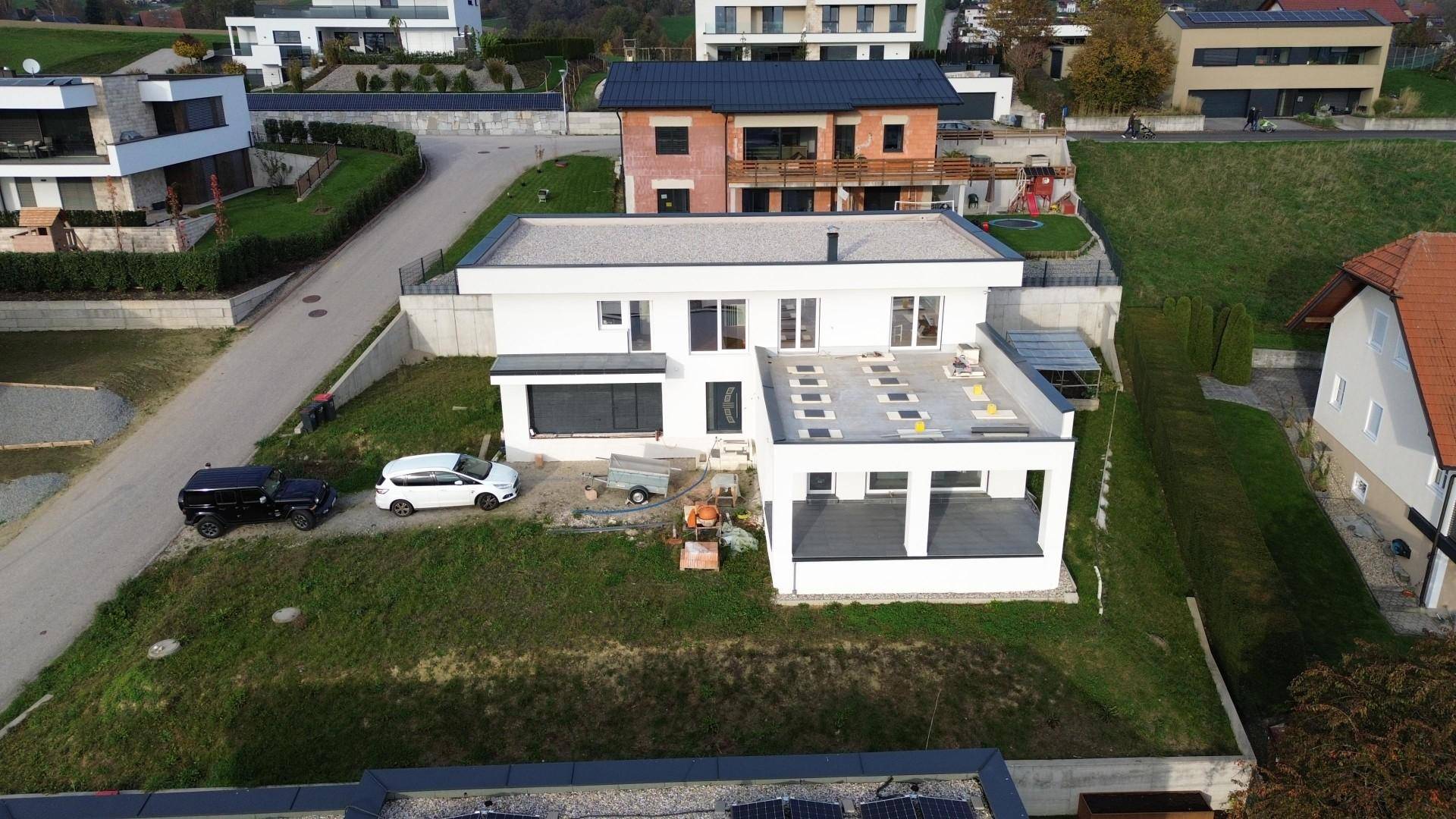 Neubau mit Flachdach und umliegenden Häusern in einer ländlichen Wohngegend.