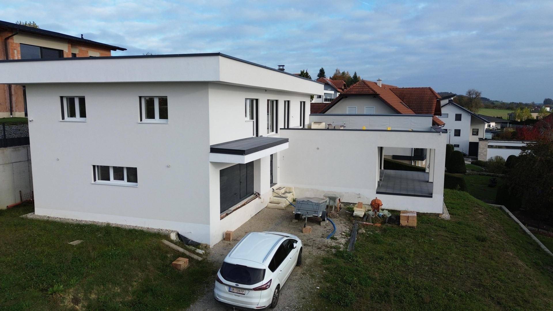 Weißes modernes Haus im Bau mit großen Fenstern und Flachdach in ländlicher Umgebung.