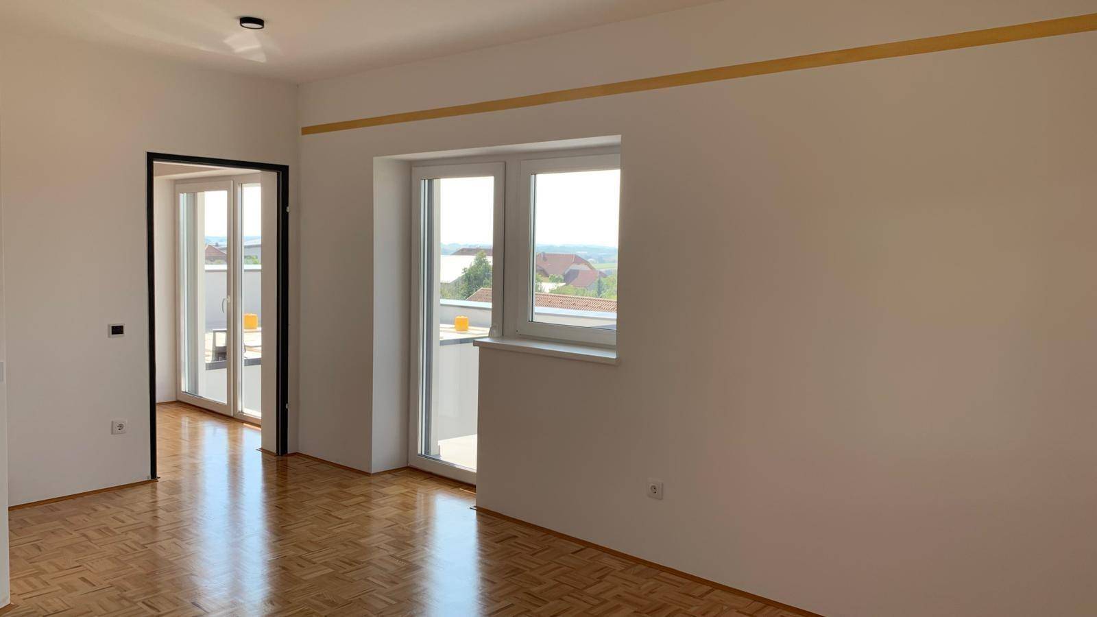 Heller Raum mit Parkettboden und Zugang zu einem Balkon, bietet weite Aussicht.