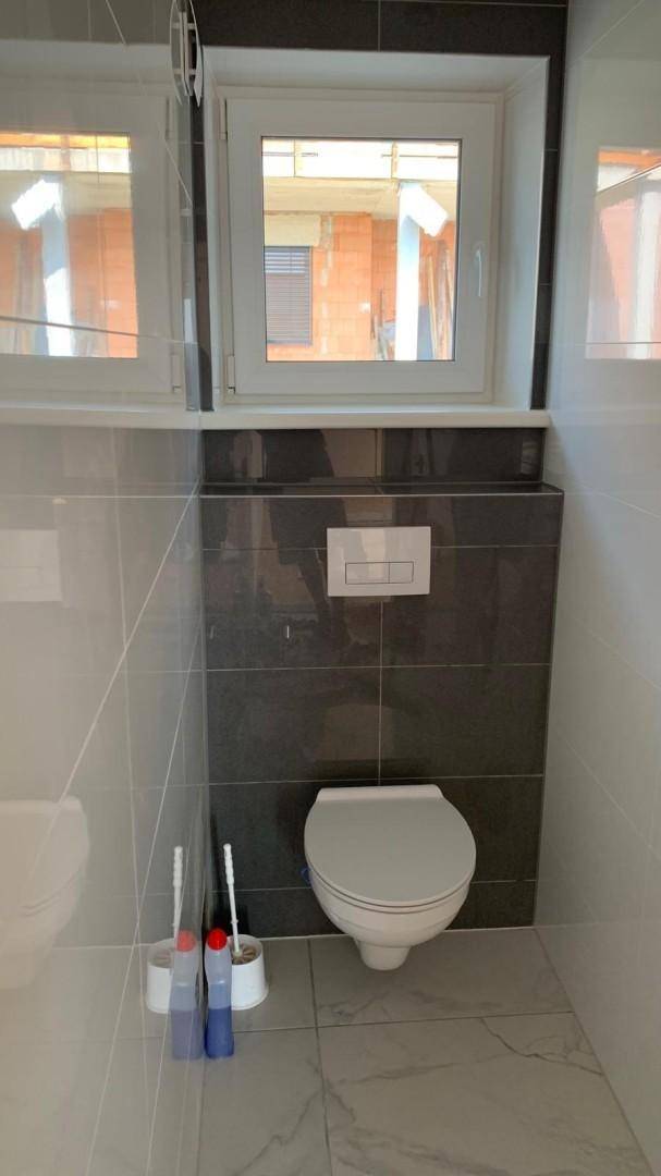 Modernes WC mit Wand-WC, Fenster und dunklen Fliesen im oberen Bereich.