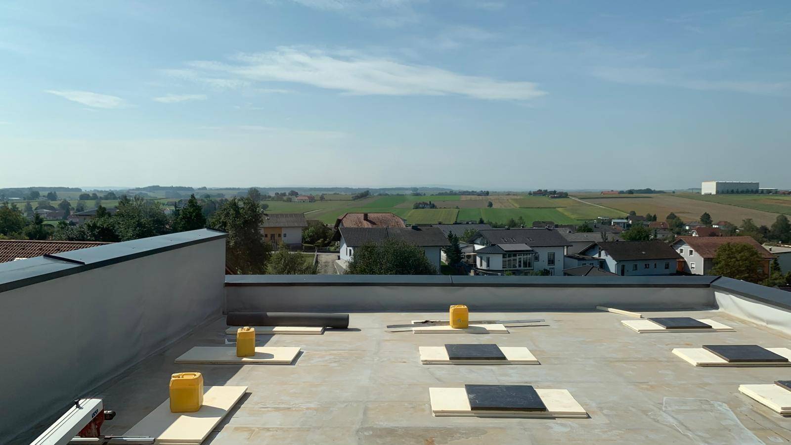 Flachdach-Terrasse im Bau mit Blick auf die umliegende Landschaft und Häuser.