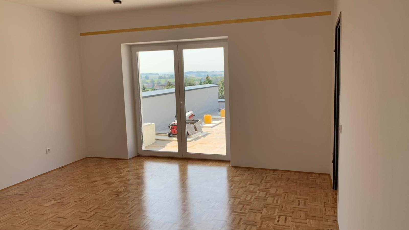 Heller Raum mit Parkettboden und Zugang zu einem Balkon, bietet weite Aussicht.