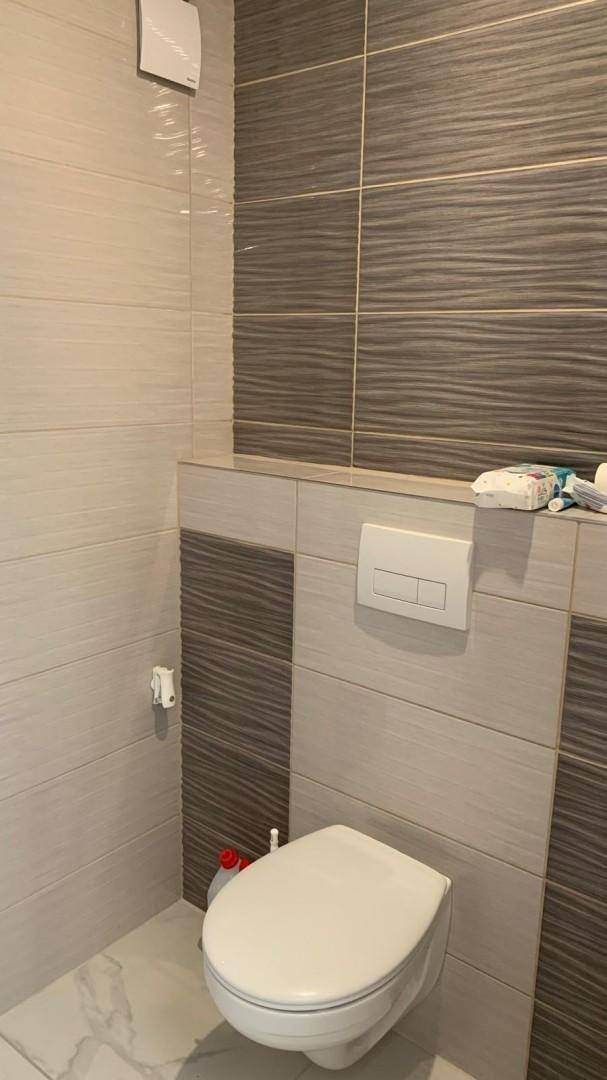 Modernes WC mit Wand-WC und stilvollen Fliesen in Grau- und Beigetönen.