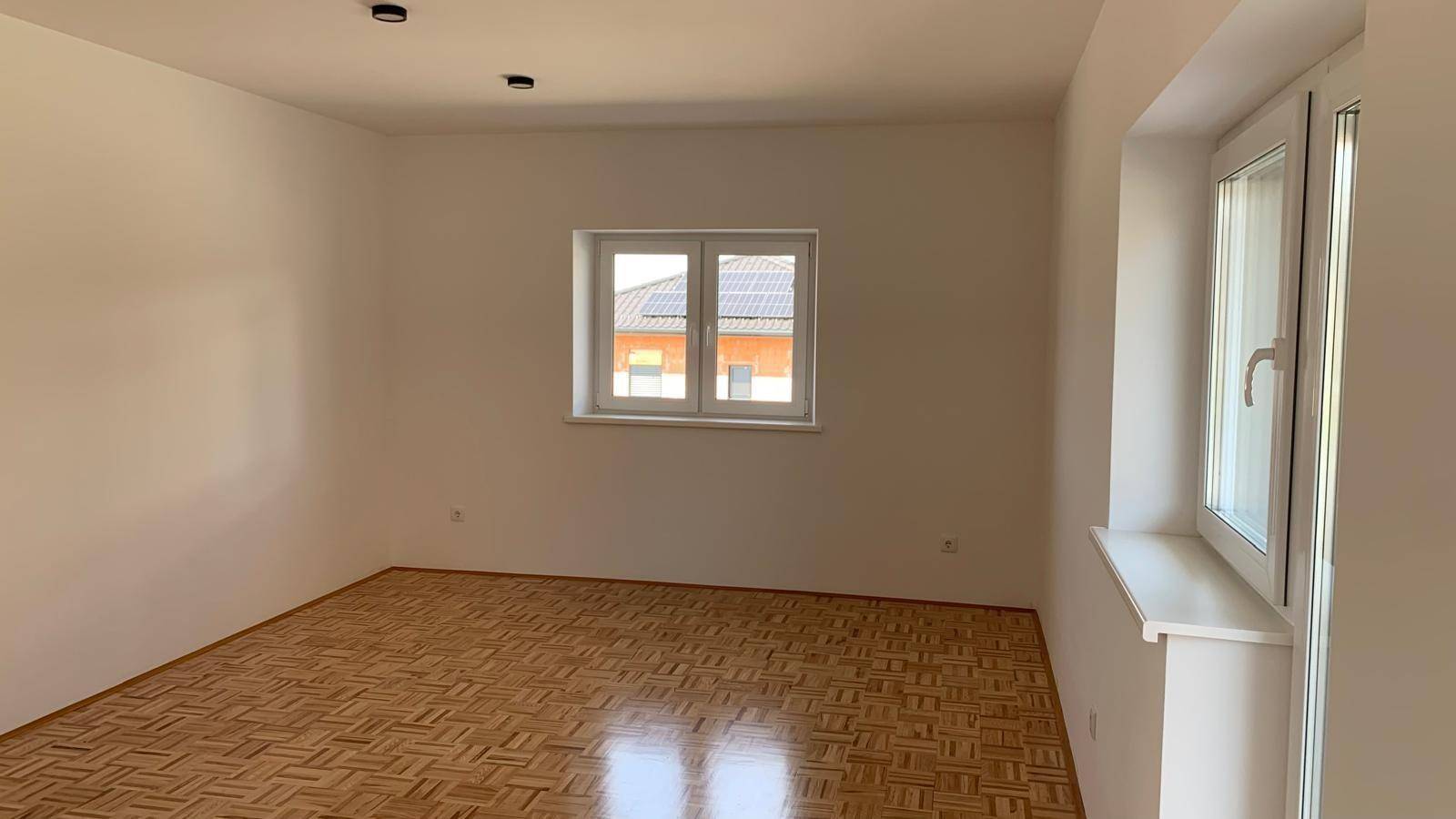 Leerer Raum mit Parkettboden und Fenster, bereit für individuelle Gestaltung.