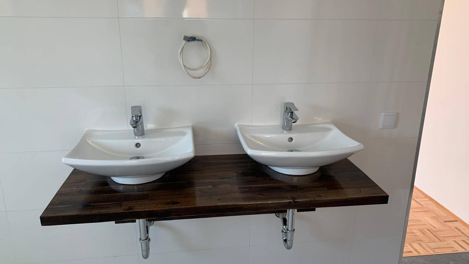 Modernes Badezimmer mit Doppelwaschbecken auf Holzplatte und weißen Wandfliesen.