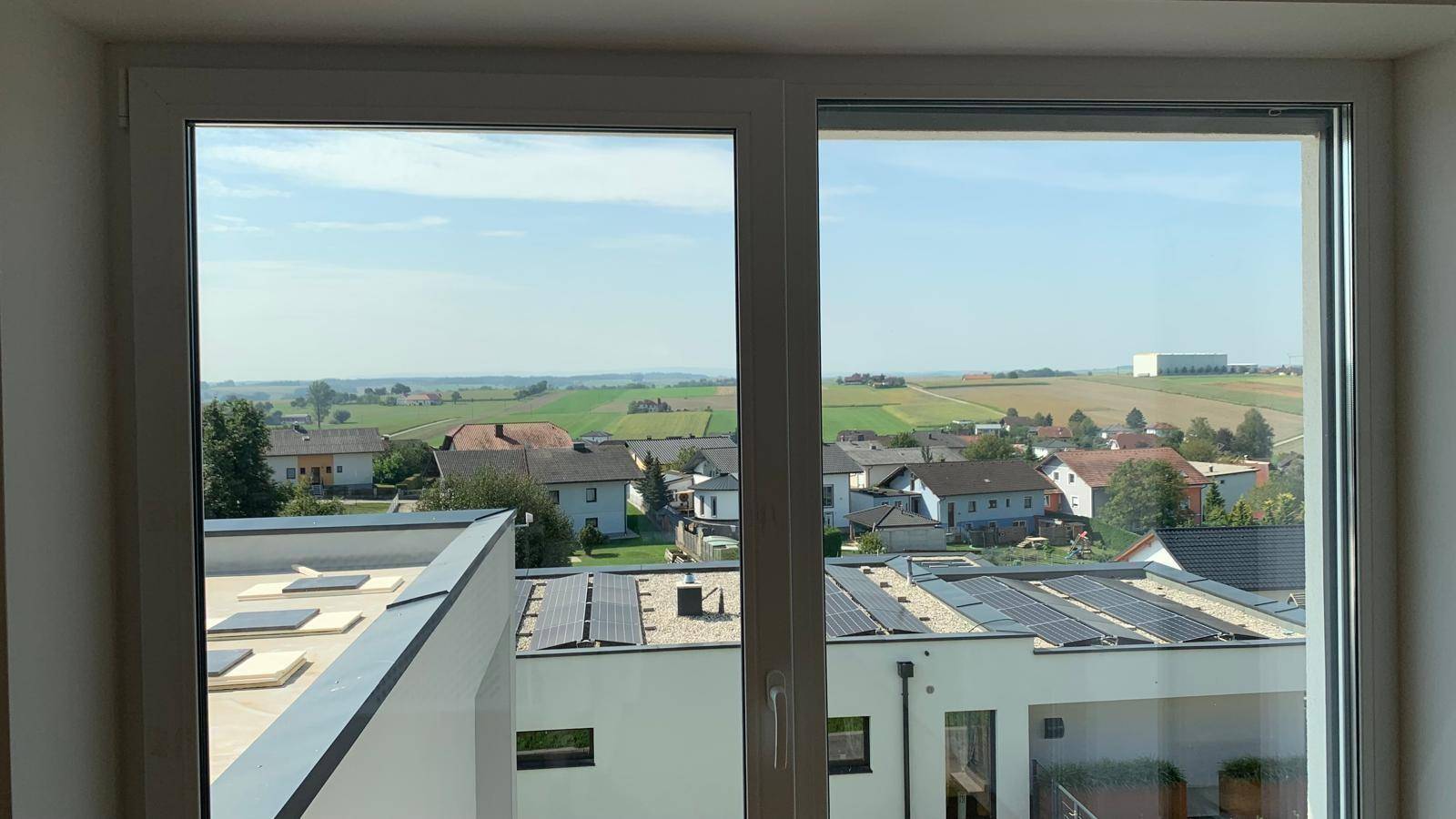 Panoramablick aus dem Fenster über die weite Landschaft und benachbarte Dächer mit Solaranlagen.