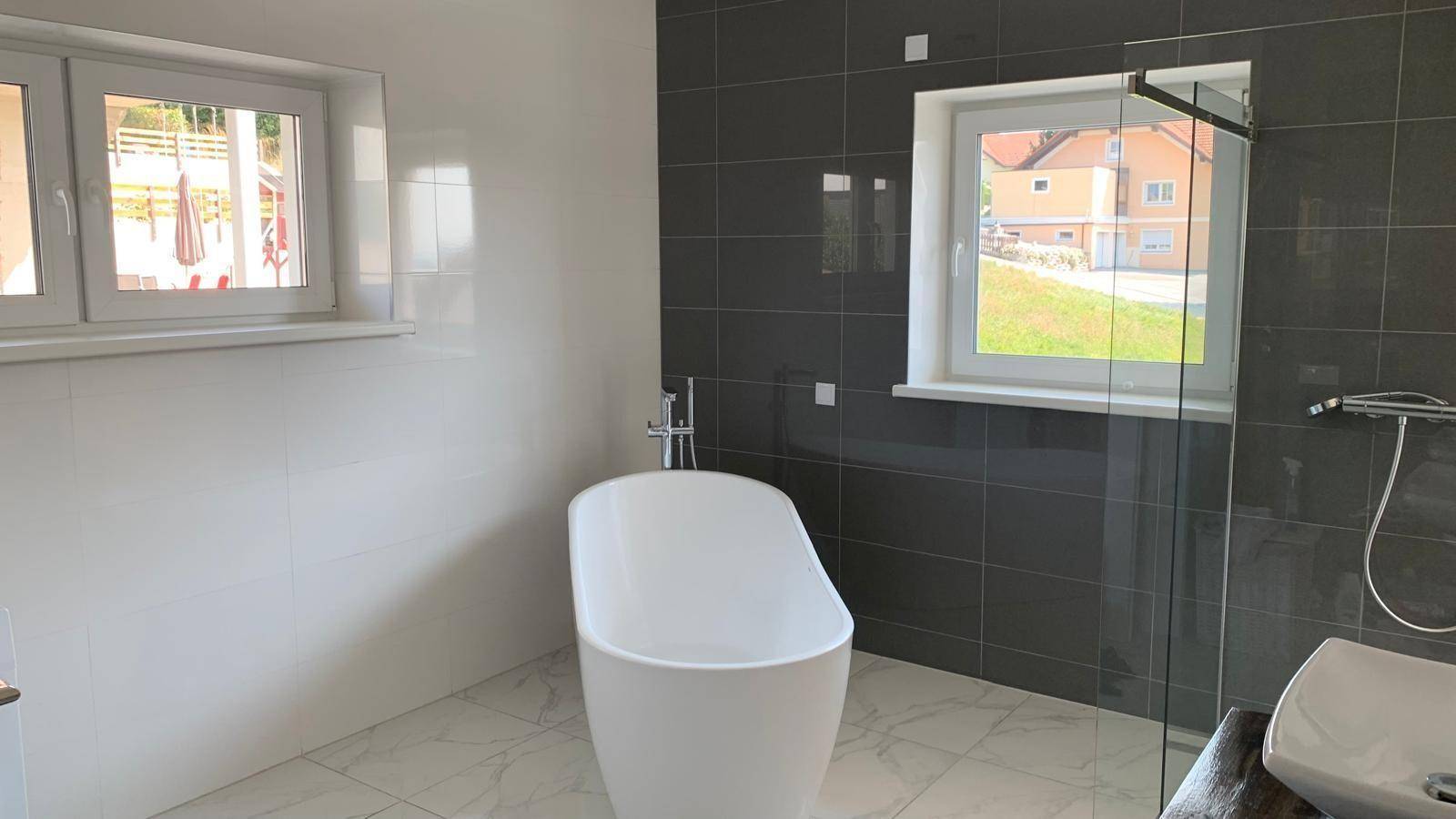 Modernes Badezimmer mit freistehender Badewanne, Dusche und zwei Fenstern.
