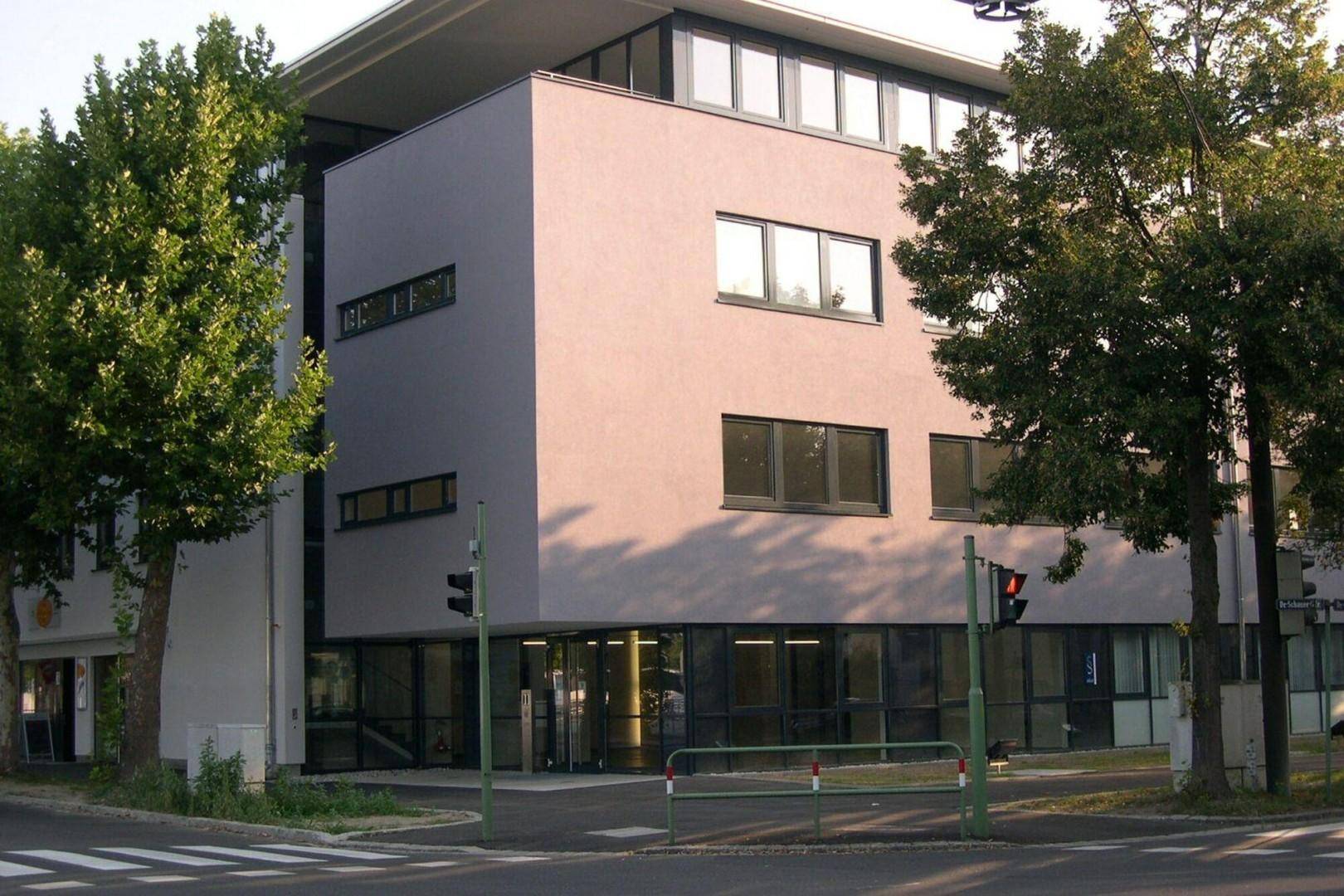 Ansicht der modernen Gebäudefassade an einer Straßenecke, umgeben von Bäumen und mit großen Fenstern.