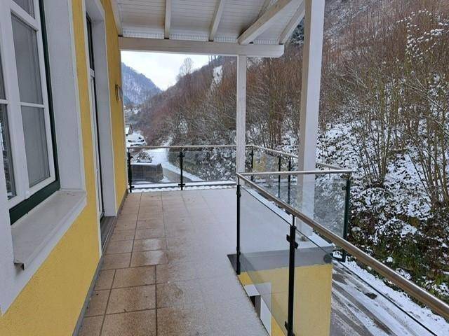 Geräumiger Balkon mit Glasgeländer und Blick auf eine verschneite Berglandschaft.