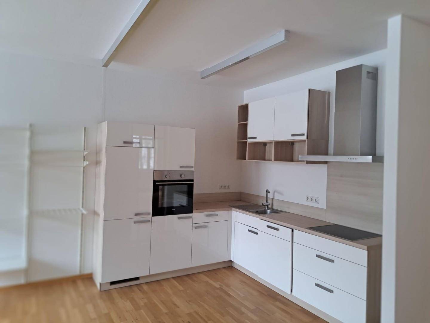 Moderne Einbauküche mit weißen Hochglanzfronten, integriertem Backofen und Dunstabzugshaube.