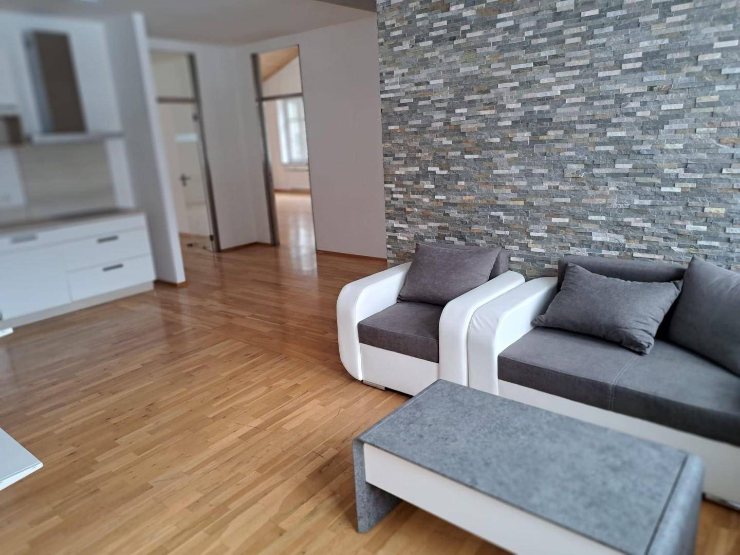 Gemütlicher Wohnbereich mit moderner Couch, Steinfassade und hellem Holzboden.