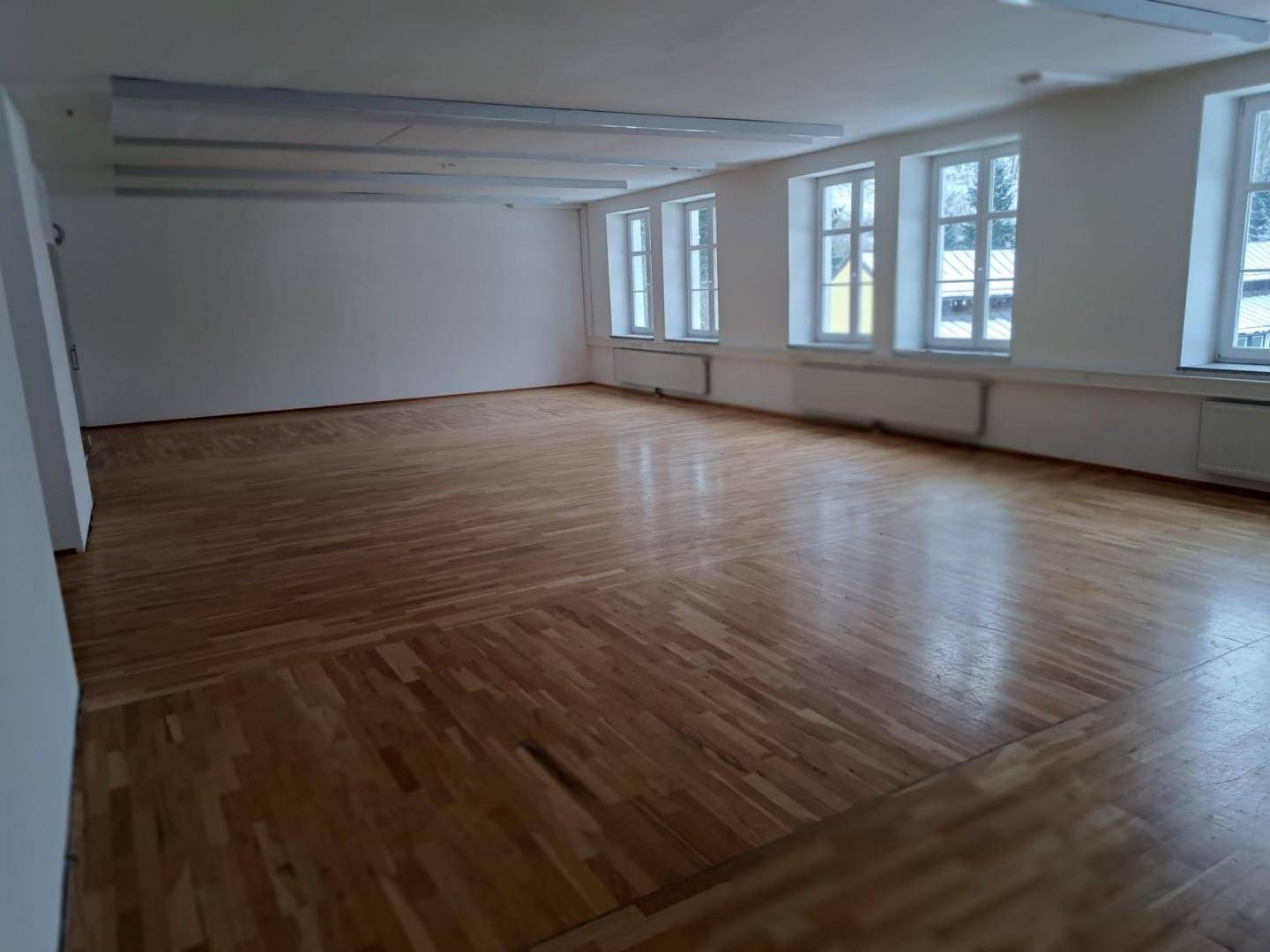 Großer, heller Raum mit vielen Fenstern und glänzendem Holzboden, ideal für vielfältige Nutzung.