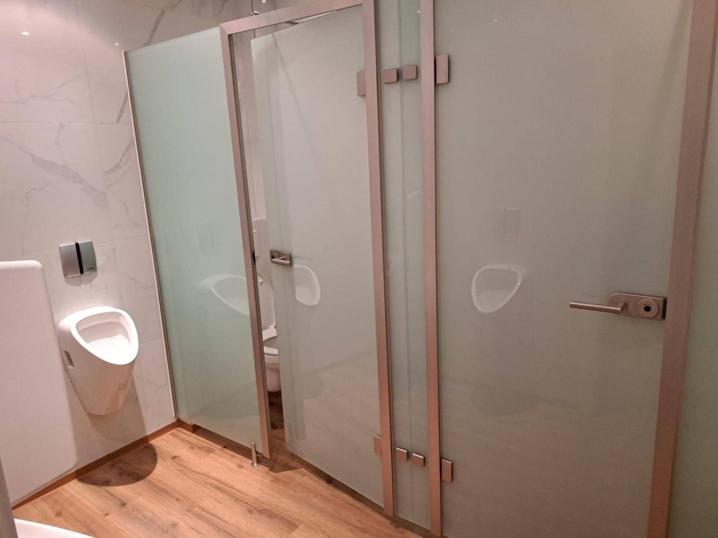 Moderner Sanitärbereich mit Urinal und abgetrennten Toilettenkabinen, ausgestattet mit Holzboden.