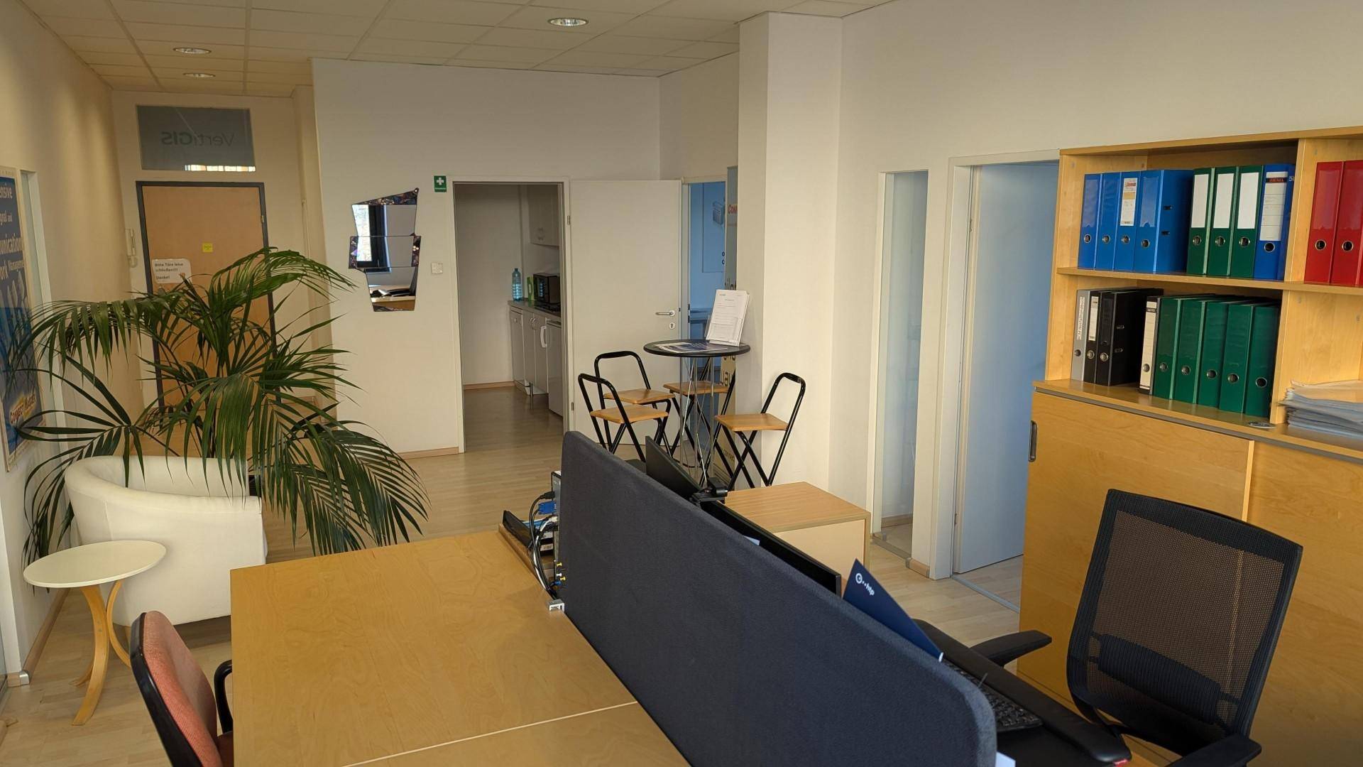 Bürobereich mit Schreibtischen, einem Wartebereich und Zugang zu weiteren Räumen im Hintergrund.