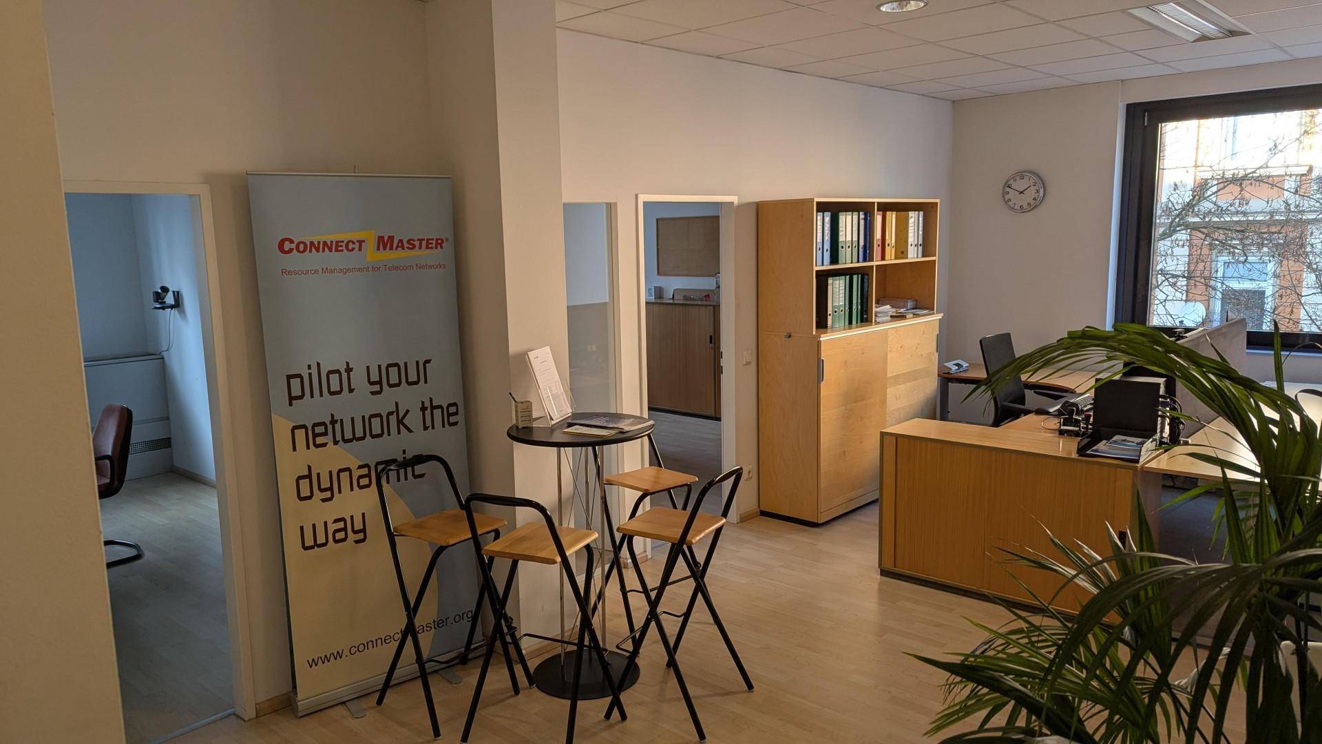 Offener Bürobereich mit Schreibtischen, einem Bücherregal und einem kleinen Stehtisch im Vordergrund.