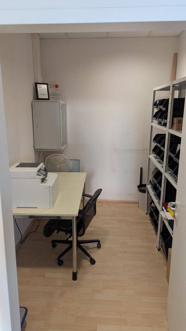 Lagerraum mit einem Schreibtisch, Drucker und Regalen für Büromaterialien und Akten.
