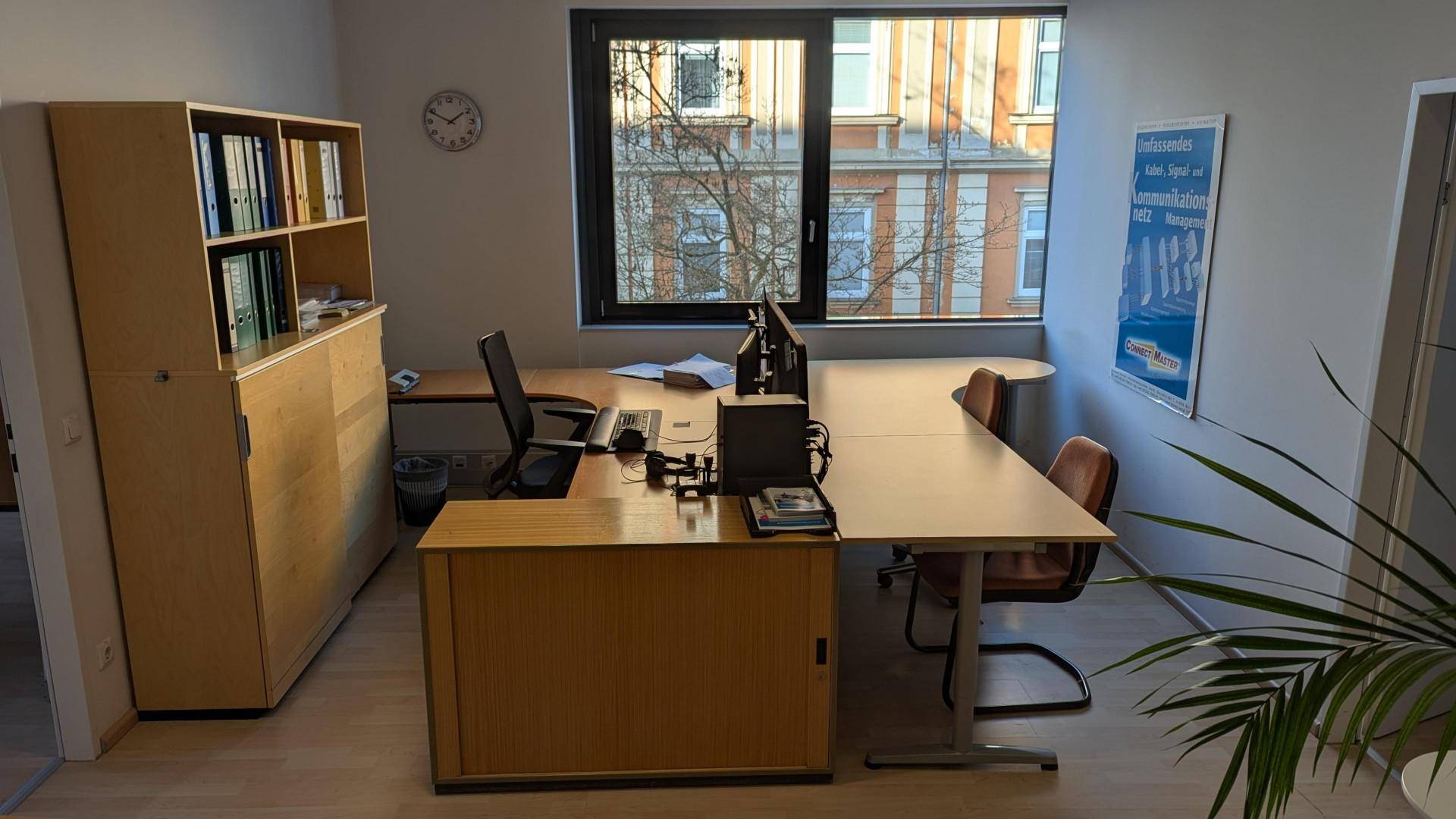 Büro mit einem großen Schreibtisch, Holzschränken und einem Fenster mit Blick auf die umliegenden Gebäude.