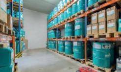 Lagerhalle mit hohen Regalen, gefüllt mit blauen Fässern und verpackten Waren auf Paletten.