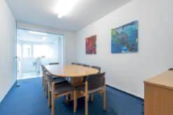 Konferenzraum mit ovalem Holztisch, mehreren Stühlen und blauer Teppichboden.